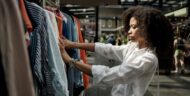 Serious curly model choosing shirts in inside flea market. There are more stalls out of focus and some people over there.